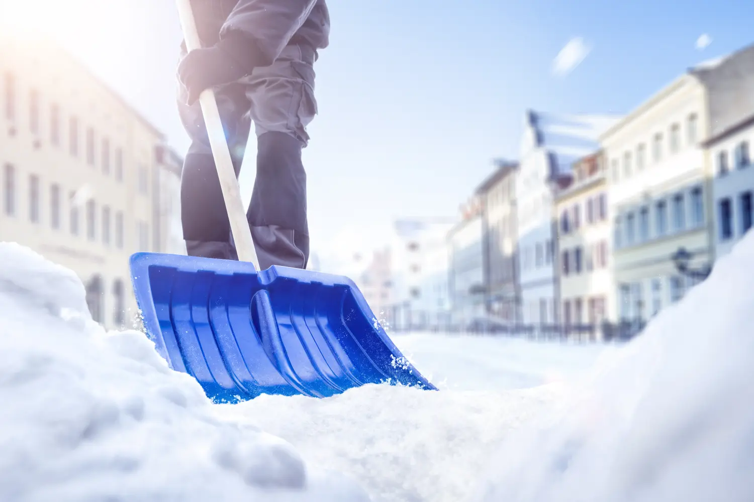 Person verwendet im Winter eine Schneeschaufel auf einer Straße